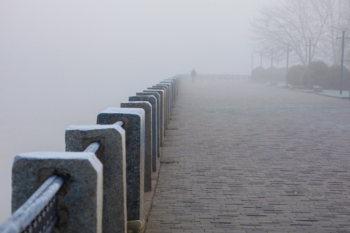 Серые стойки ограды сливаются вдали с серой брусчаткой и таким же небом