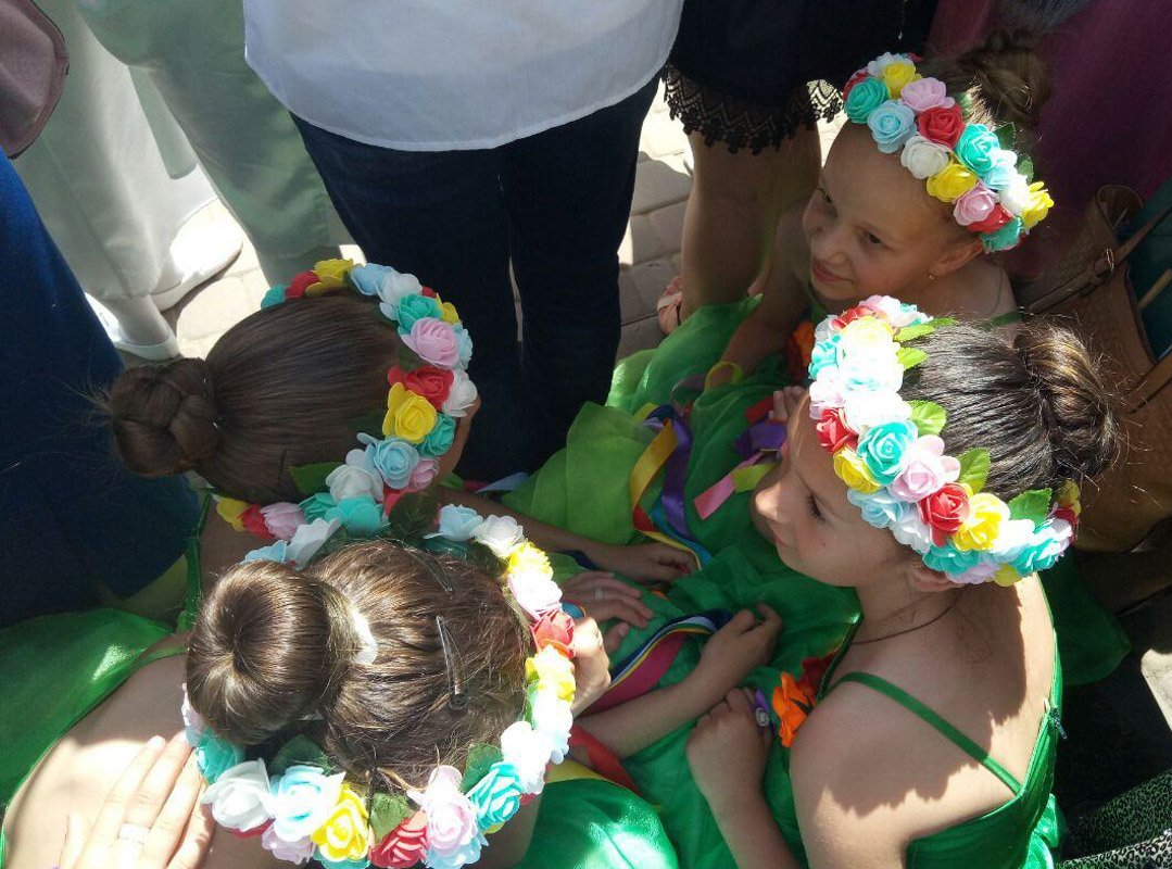 Несколько девочек, одетые в танцевальные наряды, устали и "перегрелись настолько сильно", что начали тесно ютиться на траве, в тени взрослых