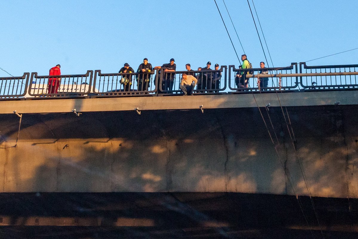 Мужчина сидел на краю моста за ограждением