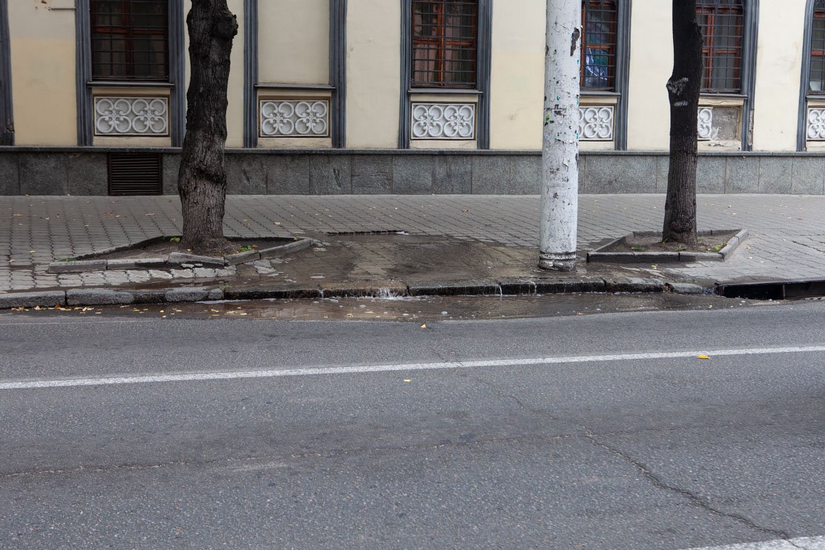 Вода вытекает из-под плитки на тротуаре