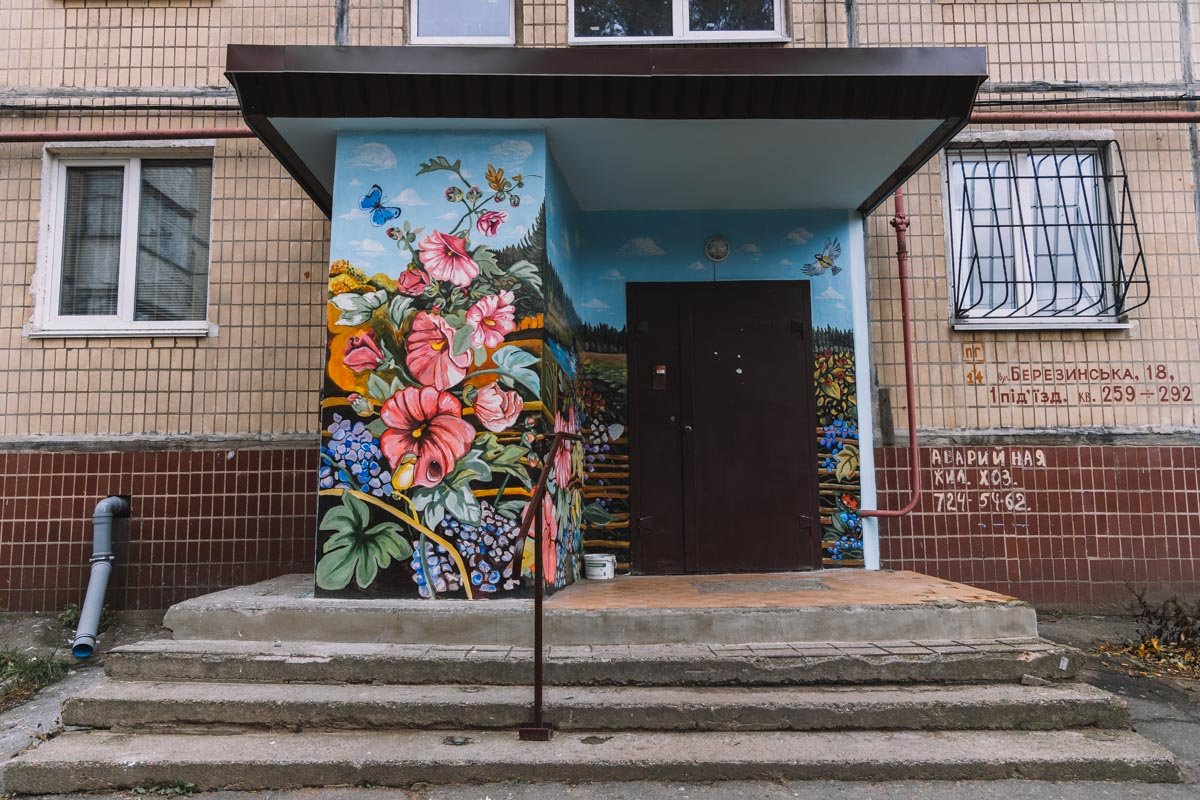 На стенах вокруг подъездных дверей появилась целая картина с изображением деревенского цветочного сада и живописной реки, уходящей к сосновому лесу