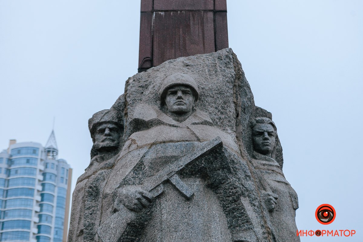 В нижней части пилона — горельефная группа из трех гранитных скульптур воинов, партизан и подпольщиков
