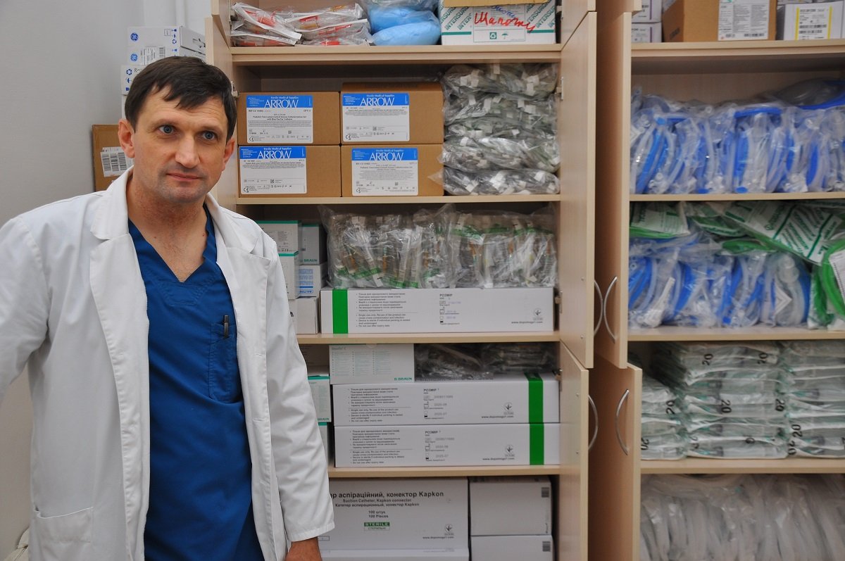 Заведующий кардиологического отделения, Олег Викторович Шашко, на фоне резервного запаса расходных материалов, приобретенных фондом “Kiddo”