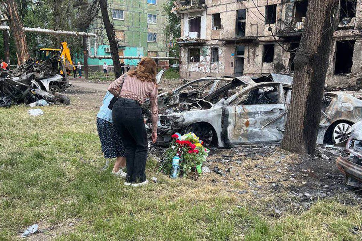 Люди несуть квіти до зруйнованого росіянами будинку 