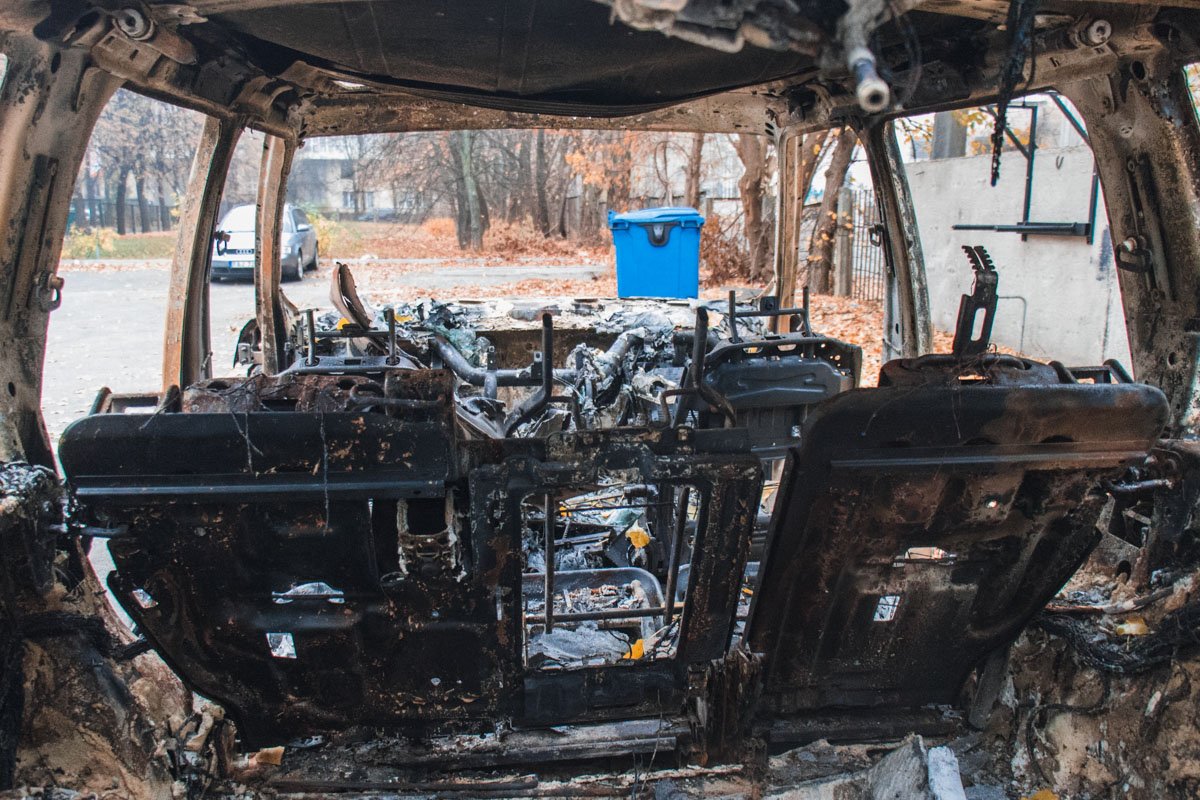 Дотла сгоревшая машина стоит на парковке здания, по какой-то причине у нее отсутствуют все четыре двери