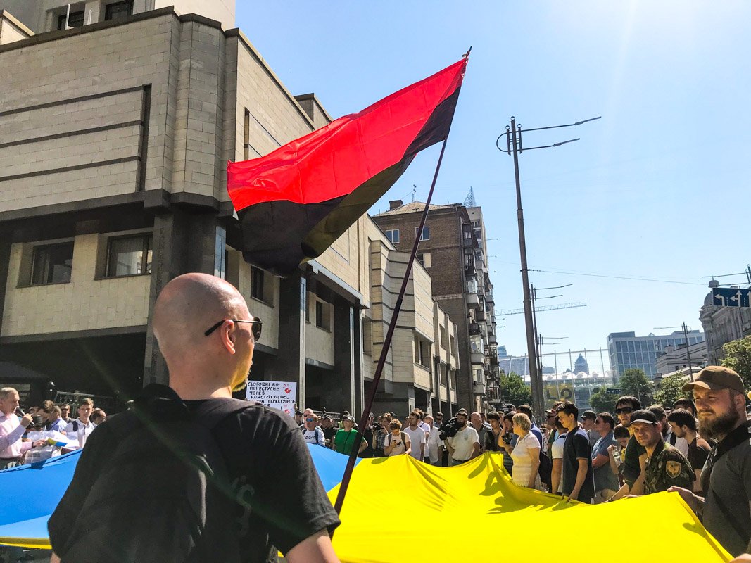 Также у здания суда стоят националисты и радикалы. В толпе заметно черно-красные знамена