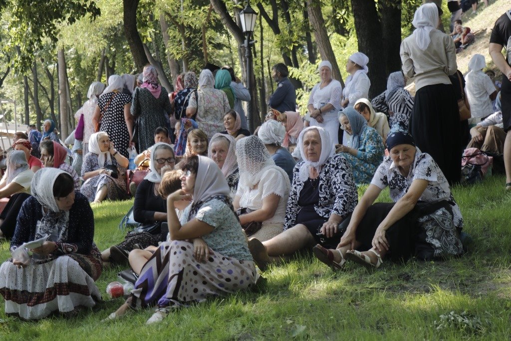 Верующие сидят на газонах в ожидании молебна