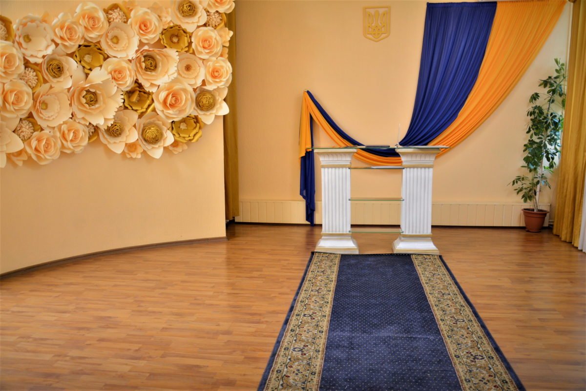 Святошинский зал для РАГС с большим флагом Украины и цветочной композицией на стене