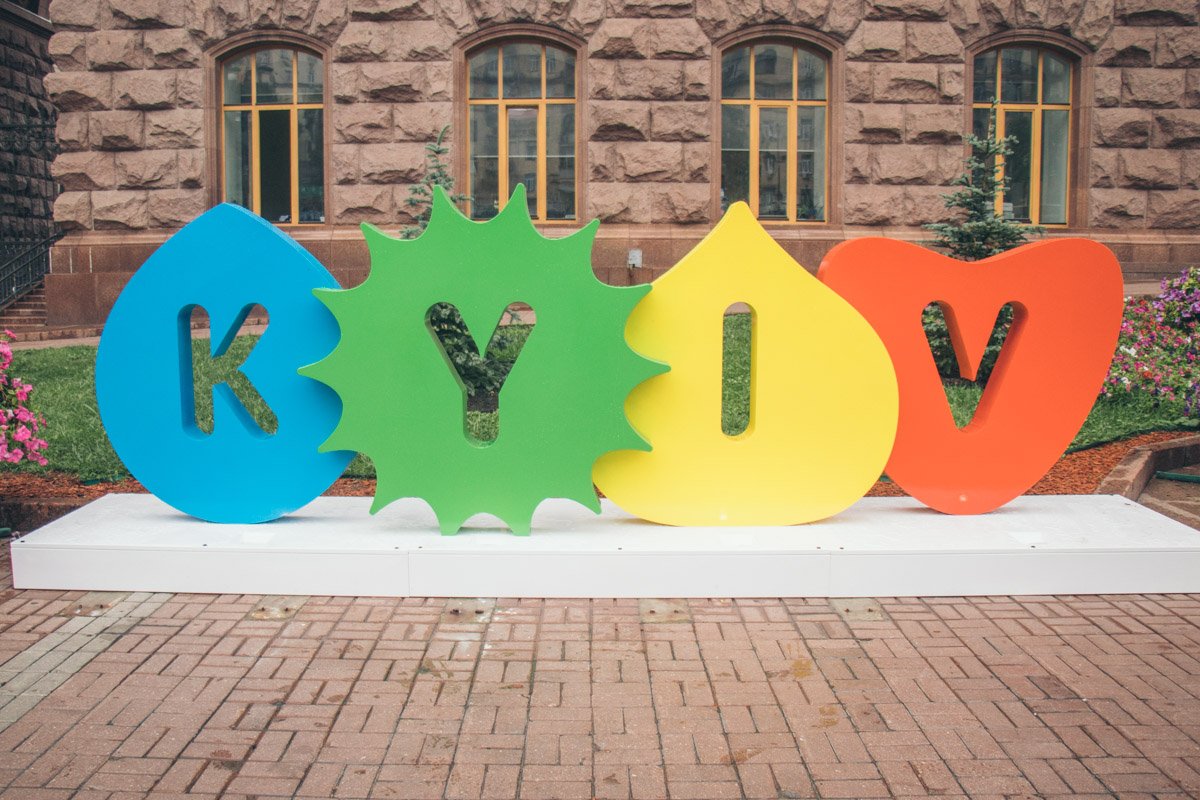 Конструкция из четырех фигурок разных цветов с надписью "Kyiv" выглядит как кусочек радуги на фоне однотонных темных стен мэрии