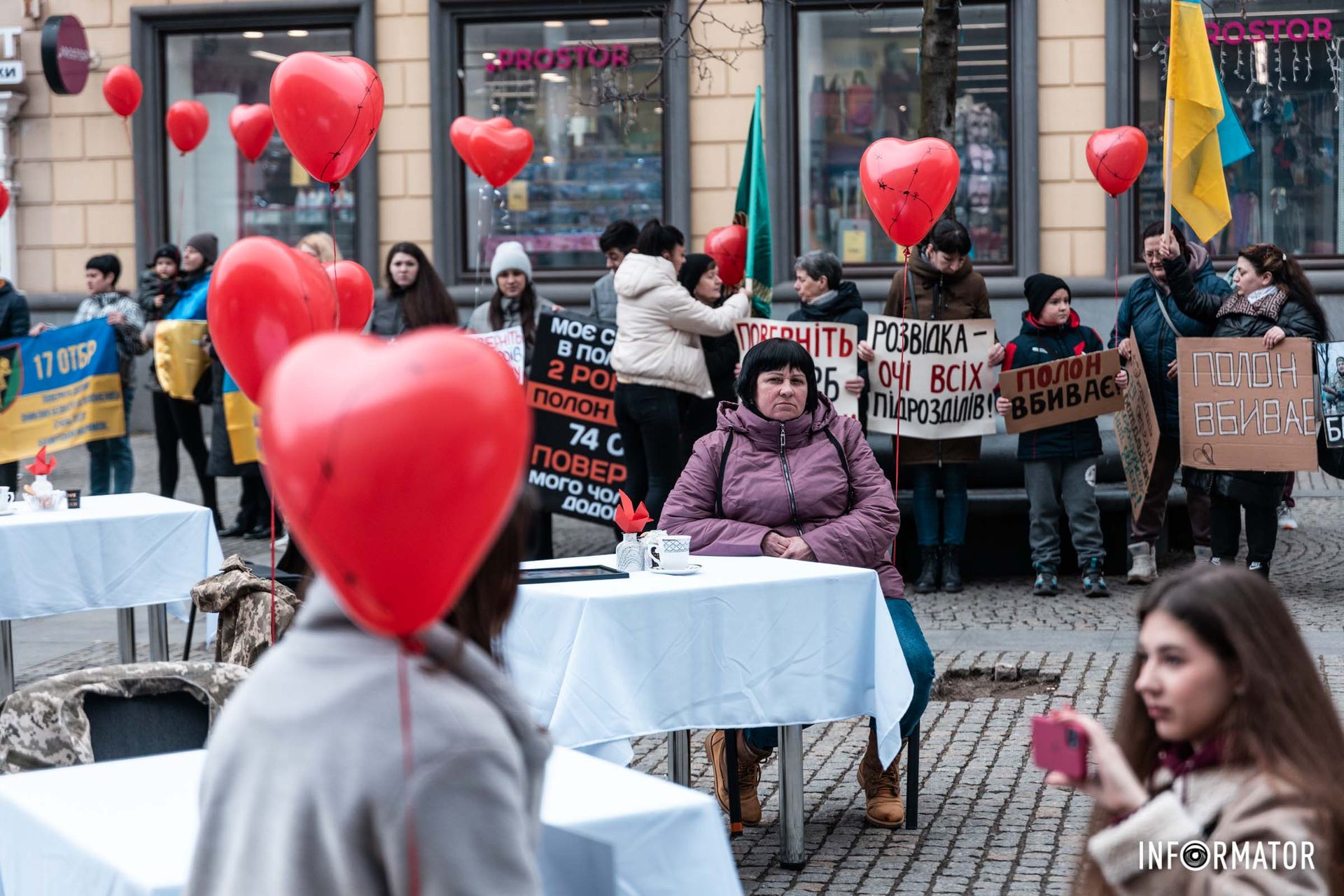 Жінки полонених сидять за столом та тримають у руках фото їхніх чоловіків Жінки полонених сидять за столом та тримають у руках фото їхніх чоловіків