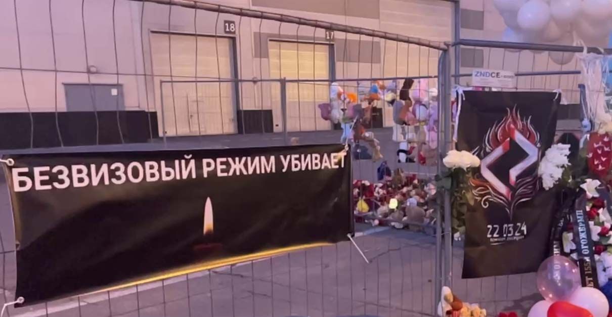 Анимигрантский баннер над стихийным мемориалом в "Крокус Сити Холли". Фото из открытых источников Анимигрантский баннер над стихийным мемориалом в "Крокус Сити Холли". Фото из открытых источников